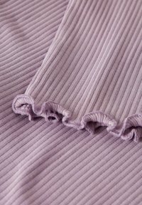 Nahaufnahme von helllila geripptem Stoff mit einem fransigen Randdetail in sanften Falten.