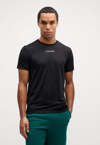 Czarna koszulka z krótkim rękawem wykonana z gładkiego, lekkiego materiału. Posiada małe białe logo "Calvin Klein" na piersi.