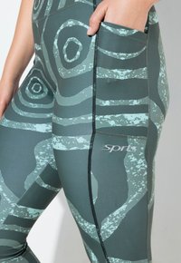 Leggings ajustados con una base verde oscuro y patrones espirales abstractos en aqua claro. Incluyen un bolsillo lateral y costuras en contraste.