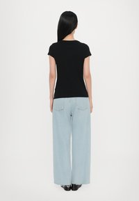 Camiseta negra de manga corta combinada con pantalones vaqueros de pierna ancha de color azul claro. Los pantalones tienen un dobladillo deshilachado y dos bolsillos traseros, completados con zapatos negros.