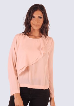 Blusa de color rosa pálido hecha de una tela suave, con un volante en un lado y mangas largas. El diseño tiene un escote redondo y un corte relajado.