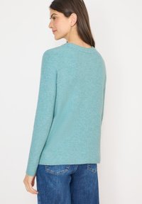 Helles blaues Strickpullover mit ribbeliger Textur, Rundhalsausschnitt und langen Ärmeln, kombiniert mit blauen Jeans.