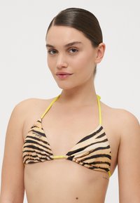 Bikini s trikotnimi skodelicami, ki vključujejo bež in črne tigerjaste proge, rumene vrvne zanke na vratu, ter nabranimi detajli iz blaga.