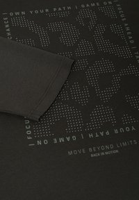 Dunkelbraunes T-Shirt mit kurzen Ärmeln, versehen mit einem strukturierten grafischen Muster und weißem, motivierendem Text in moderner Schrift.