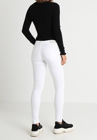 Jeans blancos ajustados hechos de denim elástico, con un diseño clásico de cinco bolsillos y una cintura de altura media, combinados con una blusa negra de canalé.