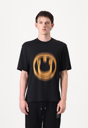 Black cotton t-shirt featuring a blurred yellow smiley face graphic at the center. Short sleeves and a relaxed fit.