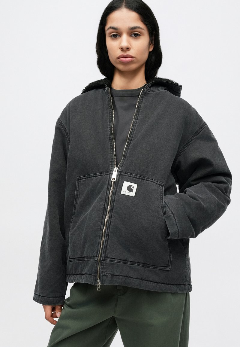 Zwarte spijkerjasje met een ritssluiting aan de voorkant, grote zakken en een gestructureerde capuchon. Voorzien van een klein logoplaatje op de borst. Casual pasvorm.