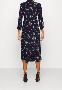 Květinové zavinovací šaty s námořnickým základem, růžovými a bílými květy, tříčtvrtečními rukávy a volným midi střihem. Nosené s černými sandály na blokovém podpatku.