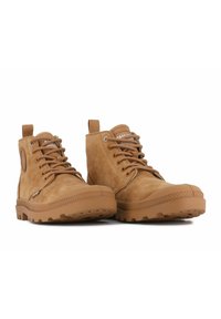 Botas de tobillo de ante marrón con cordones en la parte delantera, puntera reforzada, suela de goma texturizada y tirador trasero. Diseñadas para la durabilidad y la comodidad.
