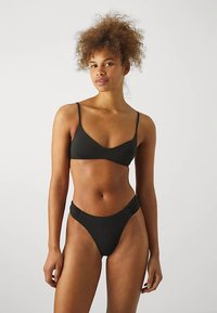 Černá bikiny souprava se trojúhelníkovou podprsenkou s tenkými ramínky a nízkým pasem kalhotek s texturovanými bočními detaily. Hladký povrch látky.