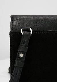 Černá kožená a semišová taška s elegantním designem, hladkou texturou a stříbrným kováním na nastavitelném popruhu.