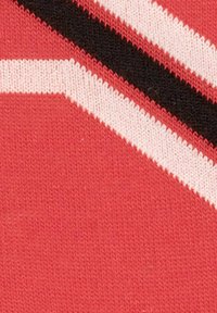 Czerwony materiał z diagonalnymi paskami w kolorze białym i czarnym, o teksturowanym wzorze dzianiny. Projekt jest odważny i geometryczny.