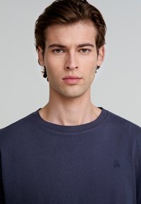 Navyblauwe katoenen t-shirt met een ronde hals en korte mouwen, voorzien van een subtiele geborduurde logo op de borst. Zachte textuur en eenvoudig ontwerp.
