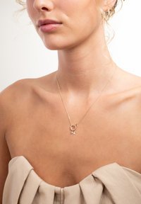 Close-up of a woman wearing a delicate gold necklace with two small star charms, dressed in a beige strapless top.
