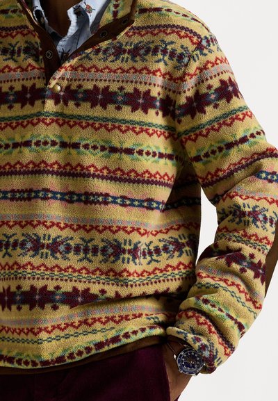 Fleece pullover in yellow with multicolored geometric patterns. Features a brown collar and snap buttons. Soft texture with long sleeves.