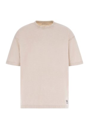 T-shirt beige à manches courtes et col rond avec un petit écusson rectangulaire près de l'ourlet inférieur sur fond blanc.