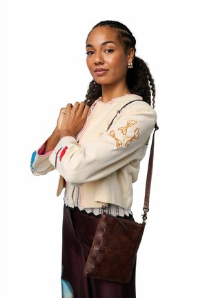 Beige geborduurde jas met kleurrijke accenten, kanten rand, gedragen over donkere, met patroon versierde broek. Bruine, gevlochten leren crossbody tas met riem.