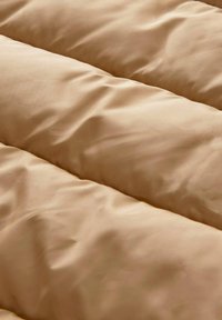 Couverture matelassée beige avec une texture lisse, présentant des motifs de couture horizontale et un tissu doux et froissé pour le confort et l'isolation.