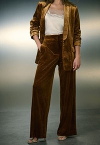 Blazer de terciopelo marrón y pantalones anchos a juego con estampado floral. Camiseta de encaje crema debajo. Sandalias con tacón bajo.