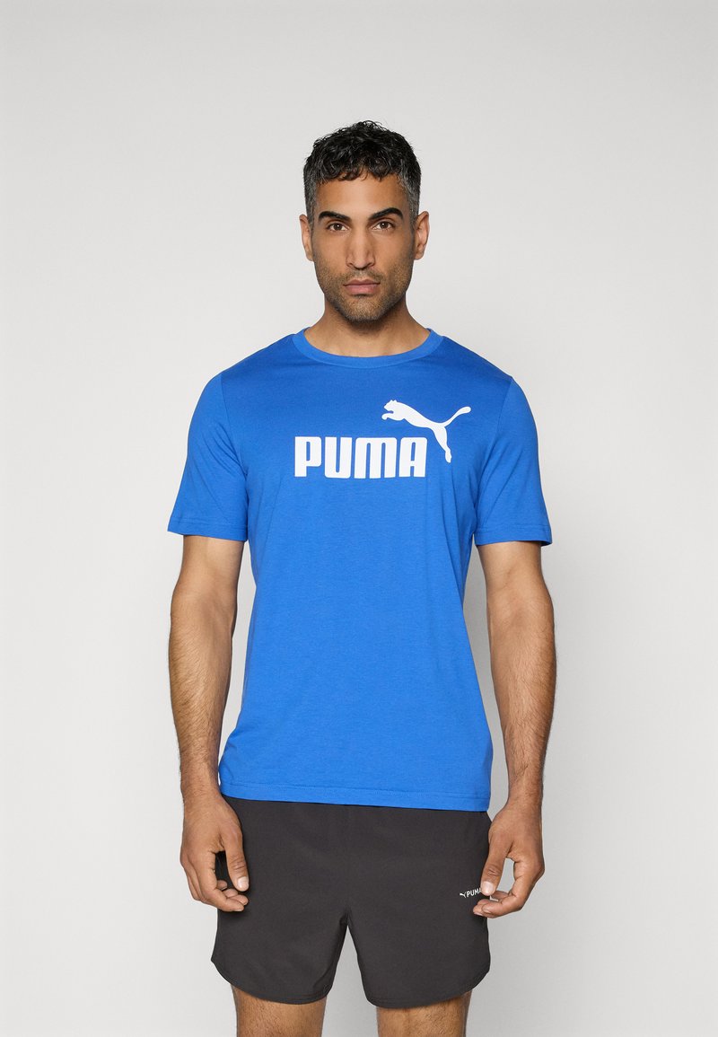 Zils īsām piedurknēm T-krekls ar baltu "PUMA" logo un kaķa emblēmu; samtaina auduma, apaļa kakla izgriezums, saskaņots ar melniem šortiem.