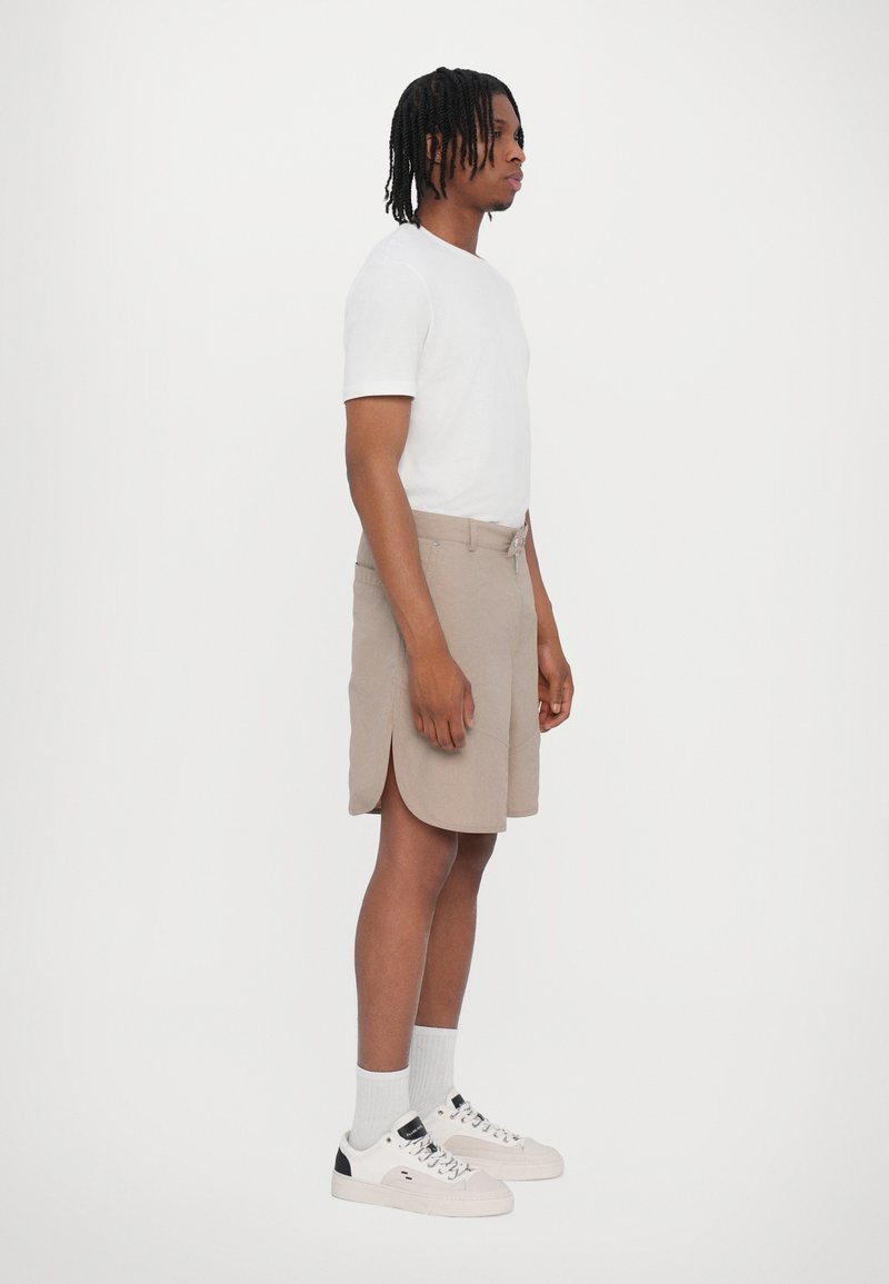 Men's white crew-neck t-shirt, paired with beige shorts featuring side slits, and white sneakers with black accents.