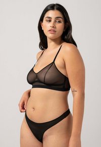 Bralette nera trasparente con spalline regolabili e coppe sagomate, abbinata a culotte alte trasparenti coordinate, caratterizzate da una texture liscia.
