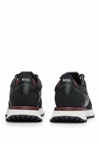 Schwarze Sportschuhe mit burgunderfarbenen Akzenten, ausgestattet mit einem glatten Lederoberteil, weißer Sohle und strukturierten Gummilaufsohlen. Markenlogo an der Ferse.