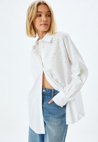 Weißes Langarmhemd mit Kragen, verziert mit geschliffenen Schmucksteinen auf der oberen Vorderseite, kombiniert mit hochgeschnittenen Denim-Jeans.