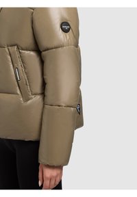 Kurtka puchowa w kolorze khaki, z połyskliwym wykończeniem, pikowaną teksturą oraz czarną naszywką z logo na rękawie. Widoczna boczna kieszeń.