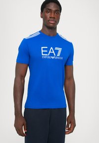 Blue short-sleeve T-shirt made from soft fabric, featuring a white logo "EA7 EMPORIO ARMANI" on the front and striped shoulder details.