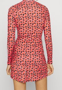 Long-sleeve red leopard print dress made of stretchy fabric, featuring a round neckline and a flared skirt. Brand logo on the sleeve.