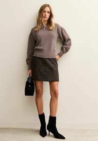Jersey marrón de punto con dobladillo acanalado, combinado con una minifalda negra con estampado de leopardo. Unos botines negros y un bolso pequeño completan el atuendo.