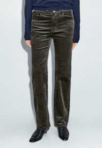 Pantaloni in corda verde scuro con vestibilità dritta, dotati di tasche laterali e una texture liscia, abbinati a scarpe nere con punta.