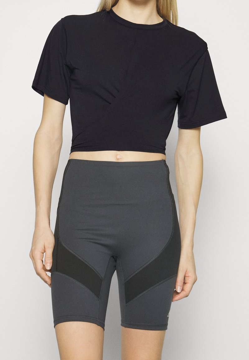 Svart kortärmad t-shirt med en vriden design. Grå höga cykelshorts med sidopaneler i en mörkare nyans.