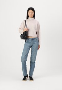 Helle rosa, gerippte Rollkragensweater, im Cropped-Format, kombiniert mit blauen geraden Jeans und schwarzen Sneakern. Schwarze Schultertasche als Accessoire.
