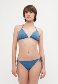 Blå bikiniuppsättning med en triangulär topp med justerbara band och en knytning på sidan. Slät textur, minimalistisk design.