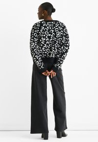 Schwarzer und weißer Leopardenmuster-Pullover mit langen Ärmeln, geripptem Saum, kombiniert mit hoch taillierten, weiten schwarzen Jeans und schwarzen Stiefeletten mit Absatz.