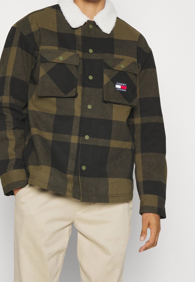 Zeleno-černá kockovaná bunda s bílým fleecovým límcem, dvěma kapsami na hrudi a značkovou nášivkou na levé straně. Texturovaná tkanina.