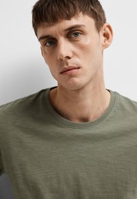 T-shirt olive green à col rond, fabriqué en tissu doux, avec une texture subtile, des manches courtes et une coupe régulière.