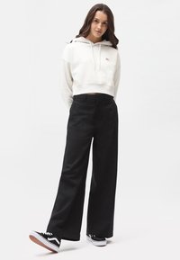 Cappuccio bianco corto con lacci, pantaloni neri a gamba larga e sneakers nere con suole bianche; tessuto morbido e vestibilità rilassata.