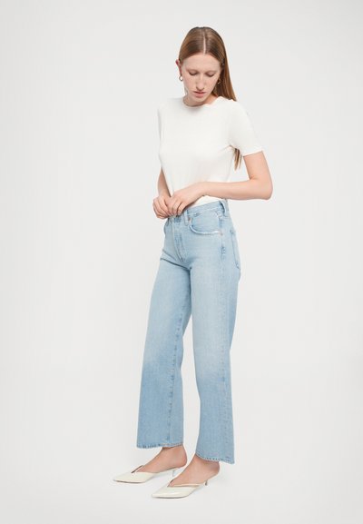 Jeans azzurri chiari a vita alta con gamba dritta, caratterizzati da un lavaggio sbiadito, design classico a cinque tasche e orlo grezzo. Abbinati a una t-shirt bianca aderente e mule color crema.
