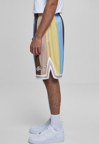 Moški atletski šortki z vertikalnimi barvnimi črtami v bež, rjavi, modri in rumeni barvi, s belim robom in logotipom, narejeni iz lahkega materiala.