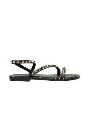 Sandali neri piatti con molteplici cinturini incrociati, adornati con borchie in metallo dorato lungo i cinturini e la suola. Realizzati in pelle liscia.