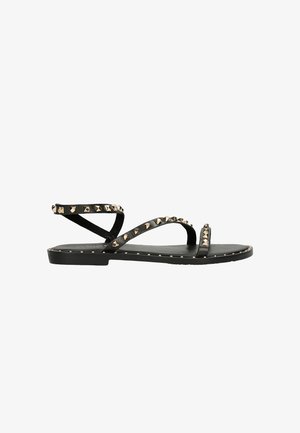Sandali neri piatti con molteplici cinturini incrociati, adornati con borchie in metallo dorato lungo i cinturini e la suola. Realizzati in pelle liscia.