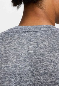 Camiseta atlética de textura gris con un cuello corto y una fila horizontal de pequeños acentos blancos en la parte trasera del escote.