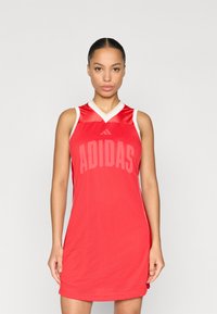 Κόκκινο φόρεμα μπάσκετ από διαπνέον ύφασμα διχτυού, με λαιμόκοψη V, λευκές λεπτομέρειες και μεγάλο λογότυπο "ADIDAS" τυπωμένο στο μπροστινό μέρος.