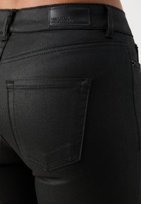 Zwarte jeans van denim, met een gladde textuur, klassieke achterzakken en een zwart leren label met "Vero Moda" branding.