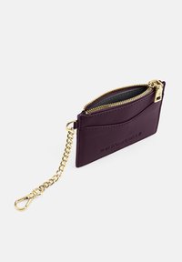 Purple leather cardholder features a zippered compartment and a gold chain with a clip. It has embossed branding and a sleek, minimalist design.