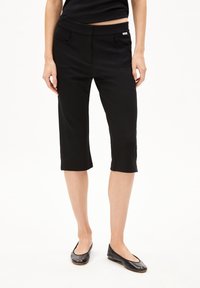 Zwarte capri-broek van een gladde, rekbare stof. Beschikt over twee voorzakken en een brede elastische tailleband voor comfort en een goede pasvorm.