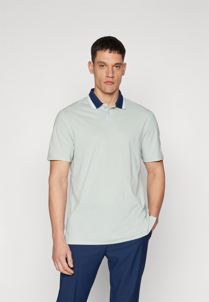 Light green polo shirt with a navy collar and white stripe. Short sleeves, soft fabric, classic fit, button placket detail, and subtle branding.